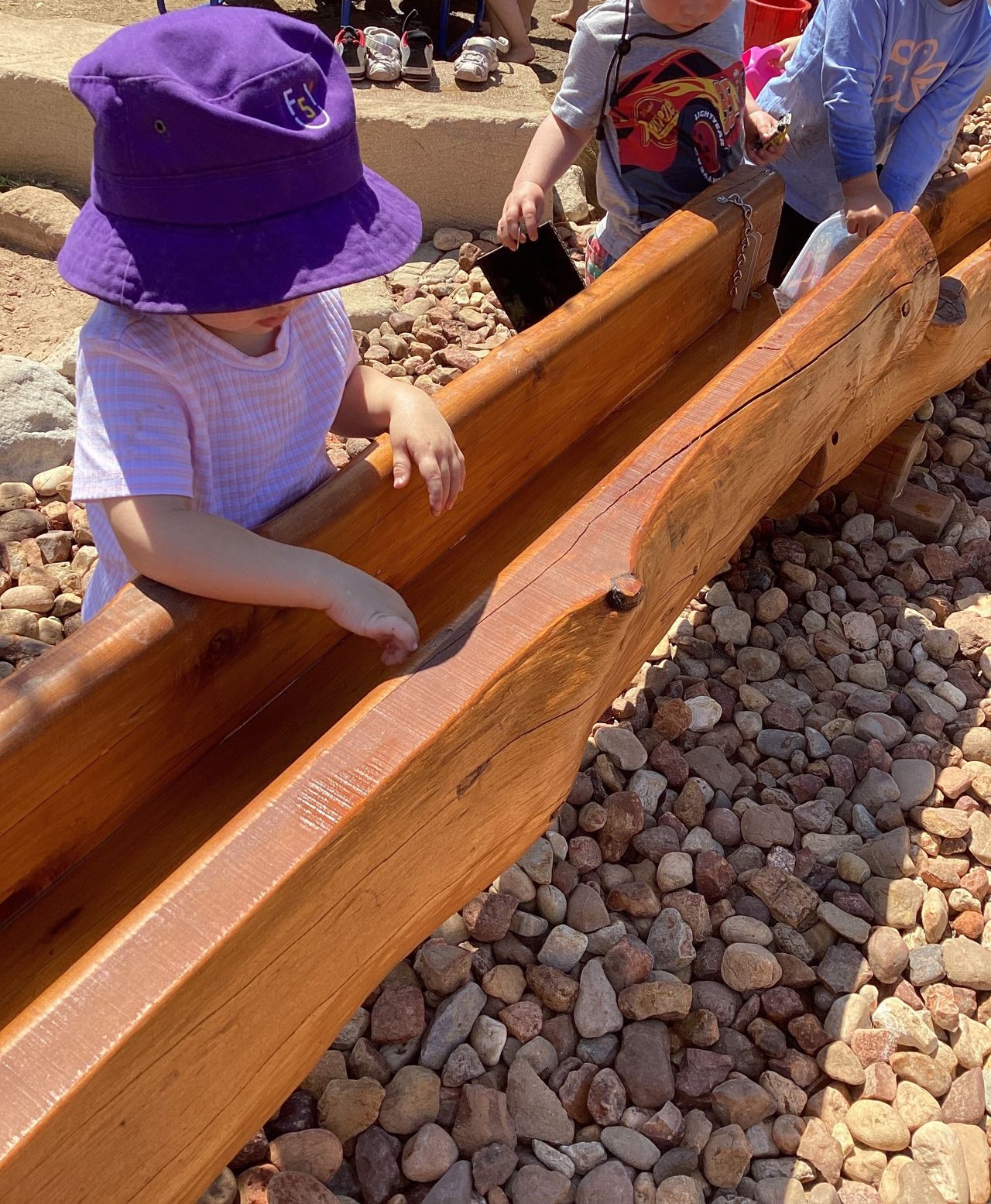 Children working together at a long timber water trough in the Emerald playscape.