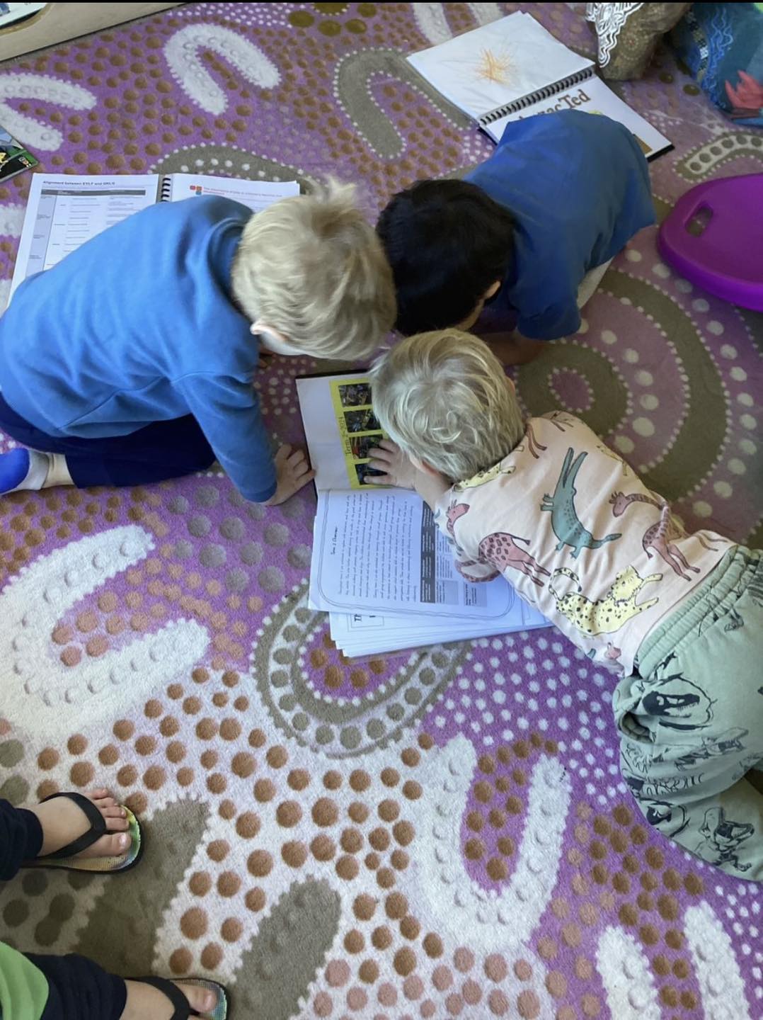 Children lying together on the floor, working over books and drawings at First5Years Emerald.
