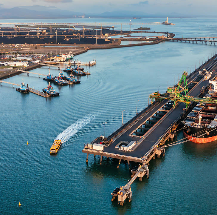 Aerial view of Gladstone harbour: tugs at their berths, the coal wharf and a ship loading beside the water.