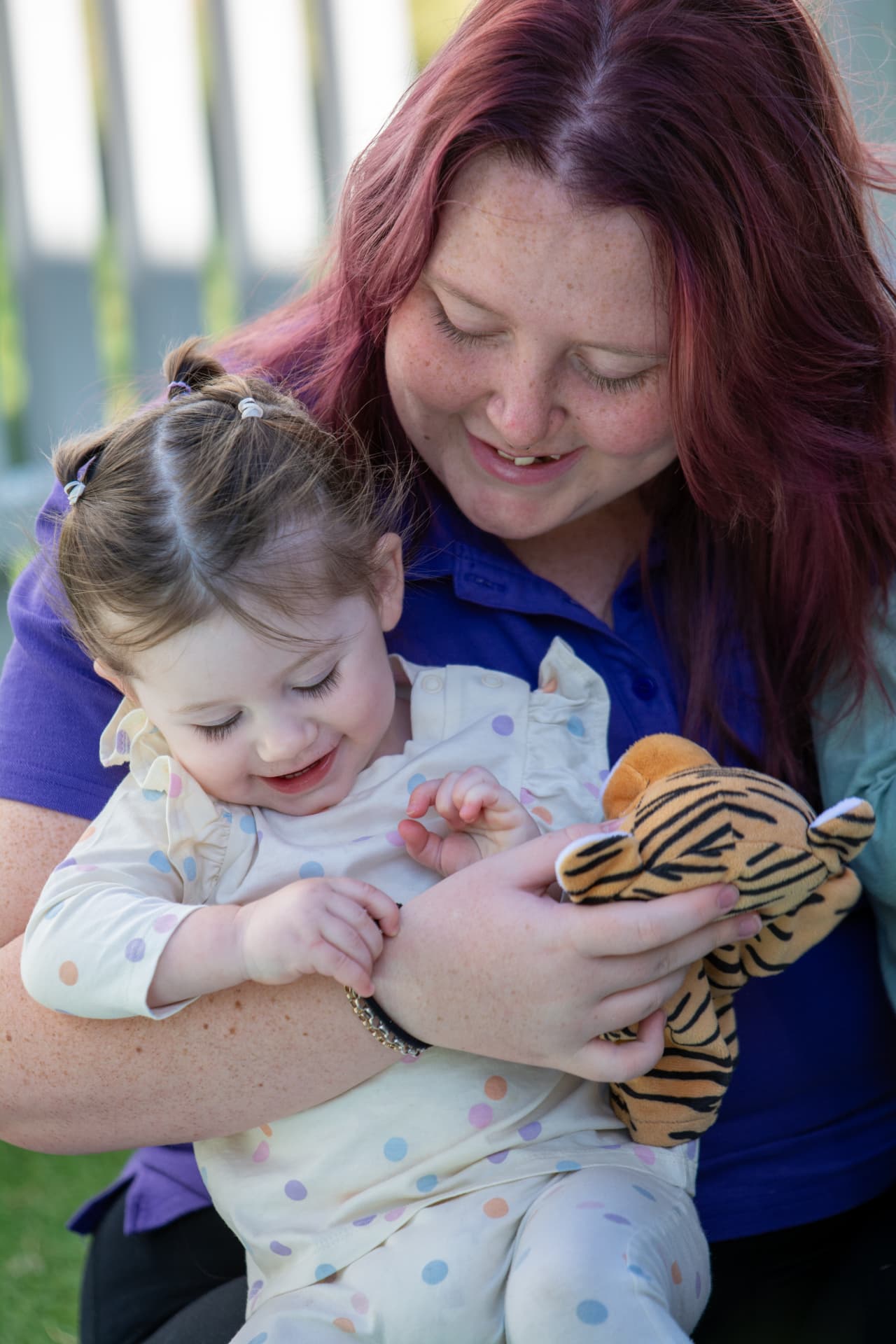 A First5Years educator holding a baby who is playing with a soft toy tiger.
