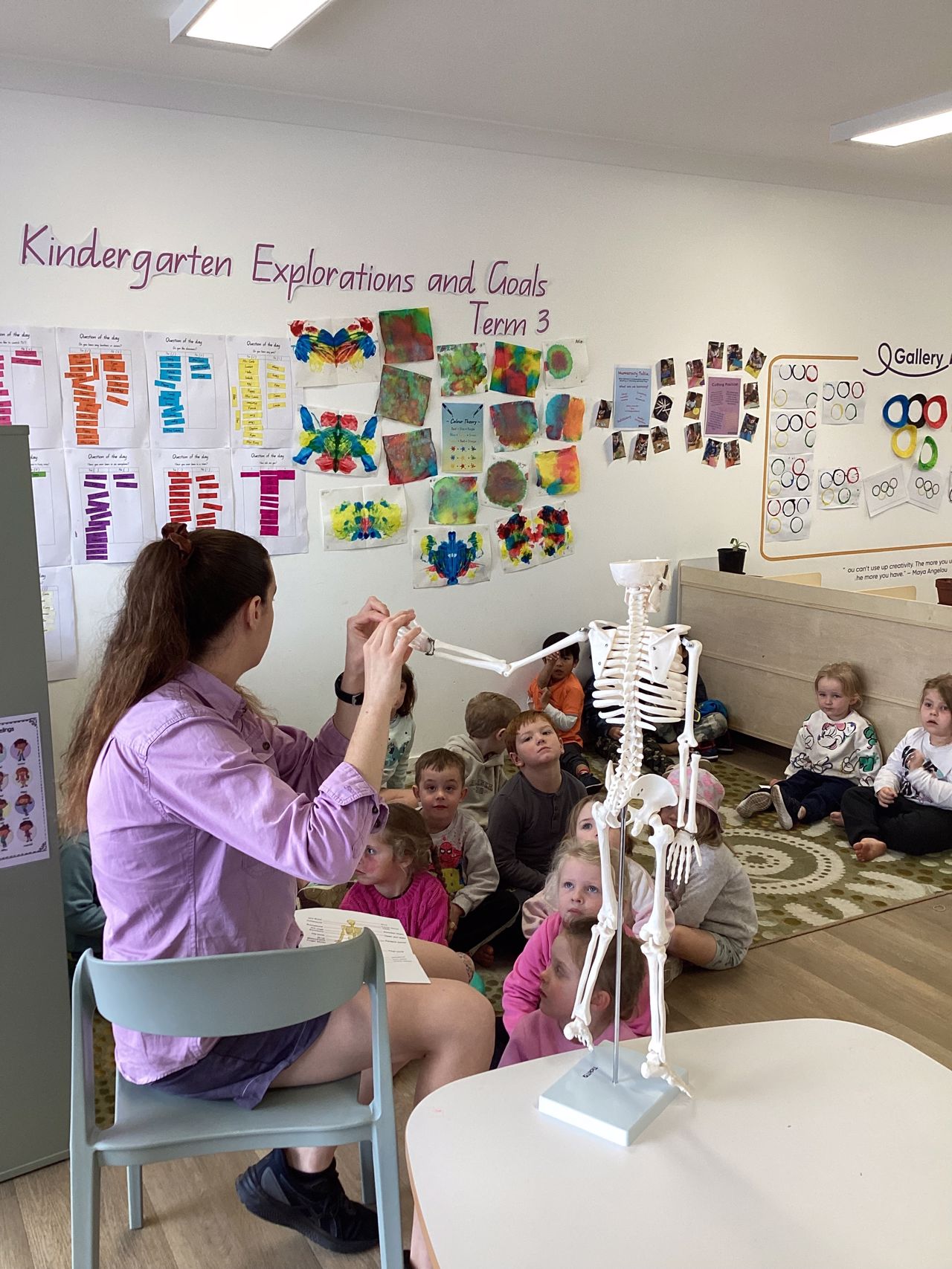 An educator and a group of Kindy children examining a model skeleton together.
