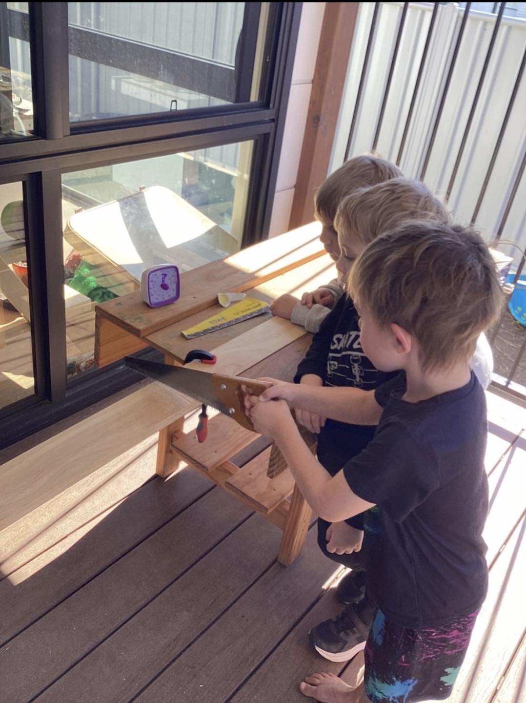 A child using a real handsaw at a work bench at First5Years Emerald, closely supervised.