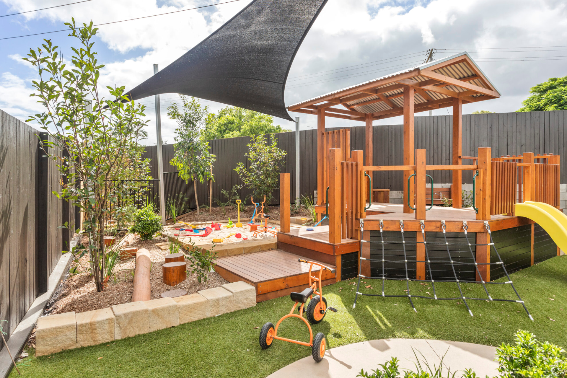Timber outdoor playscape at First5Years Calliope with a deck, cargo net, sandpit and planting.