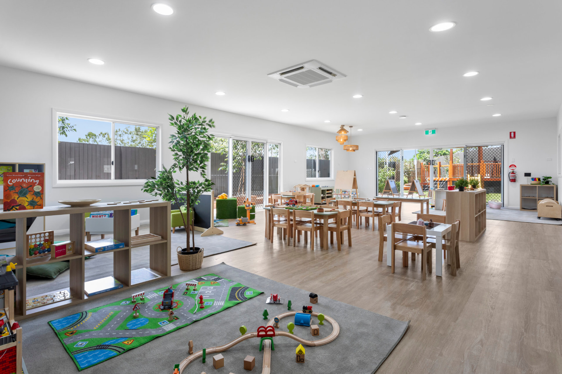 A wide First5Years Calliope studio with timber tables, a road rug and doors opening to the yard.